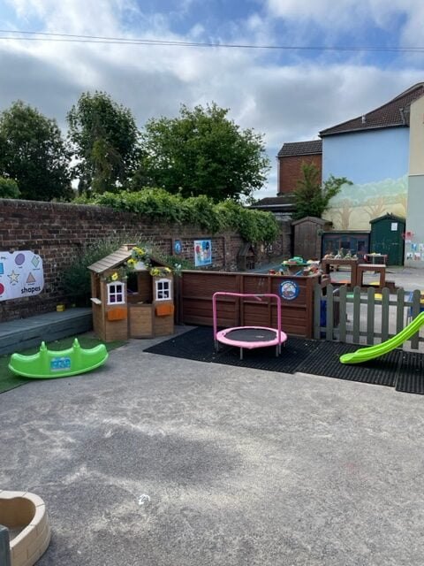 Garden play area with a wooden playhouse, a pink trampoline and a green slide
