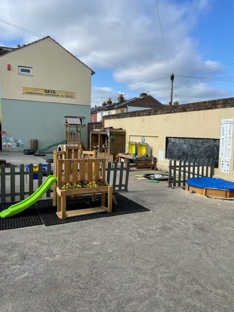 Garden with a green slide, a flower planter, a chalkboard wall and a sandpit