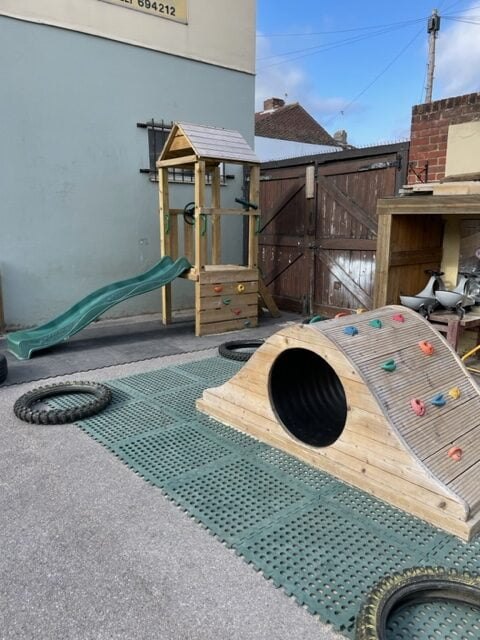 Climbing frame with a slide and a wooden climbing tunnel on safety matting
